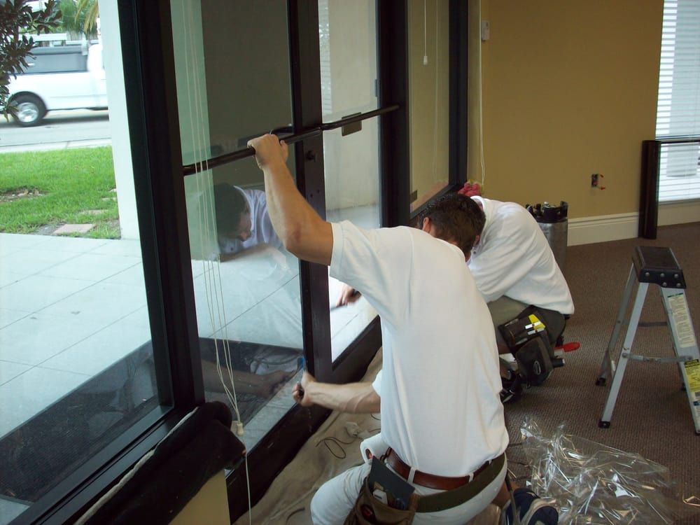 Worker in a white t-shirt kneeling and working on a large glass door frame